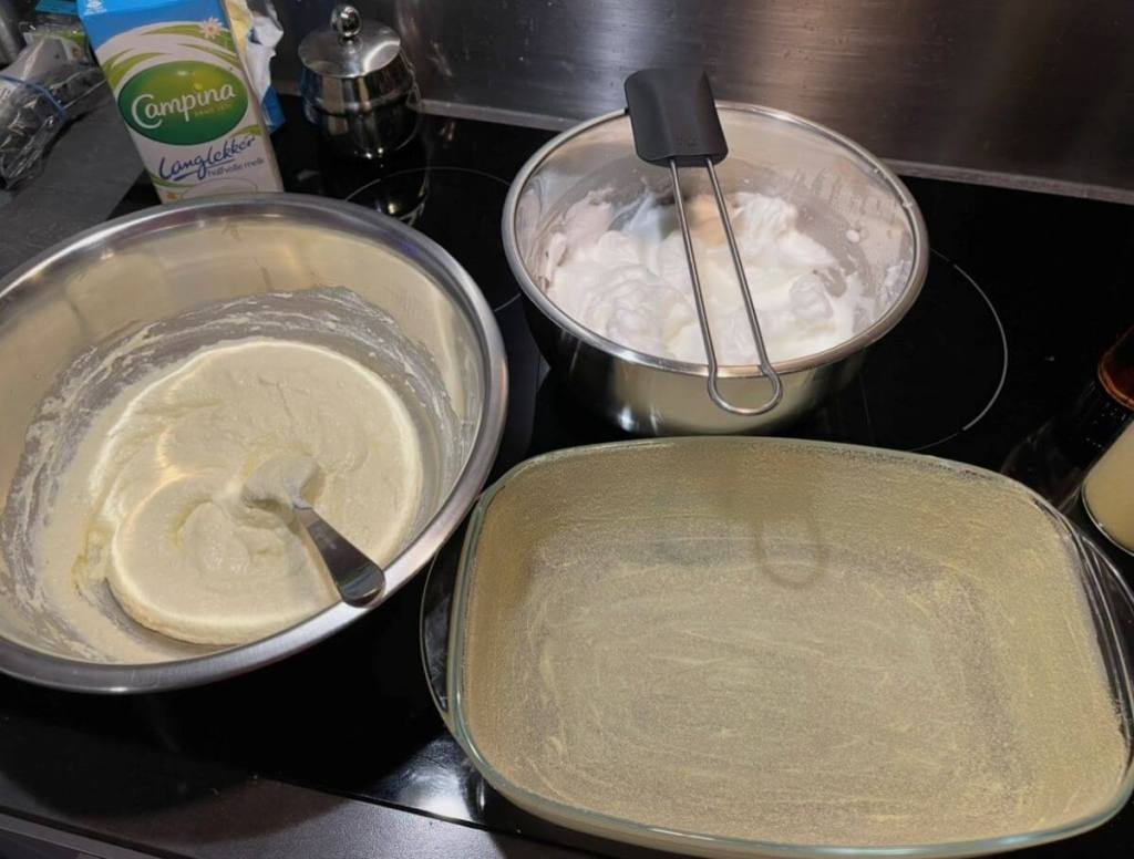 Išplakti kiaušinių baltymai dubenėlyje, varškės ir kitų ingredientų mišinys dubenyje, o kepimo indas pabarstytas manais.