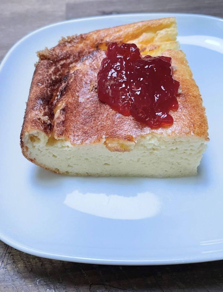 Atpjautas varškės apkepo gabalėlis su uogiene lėkštėje