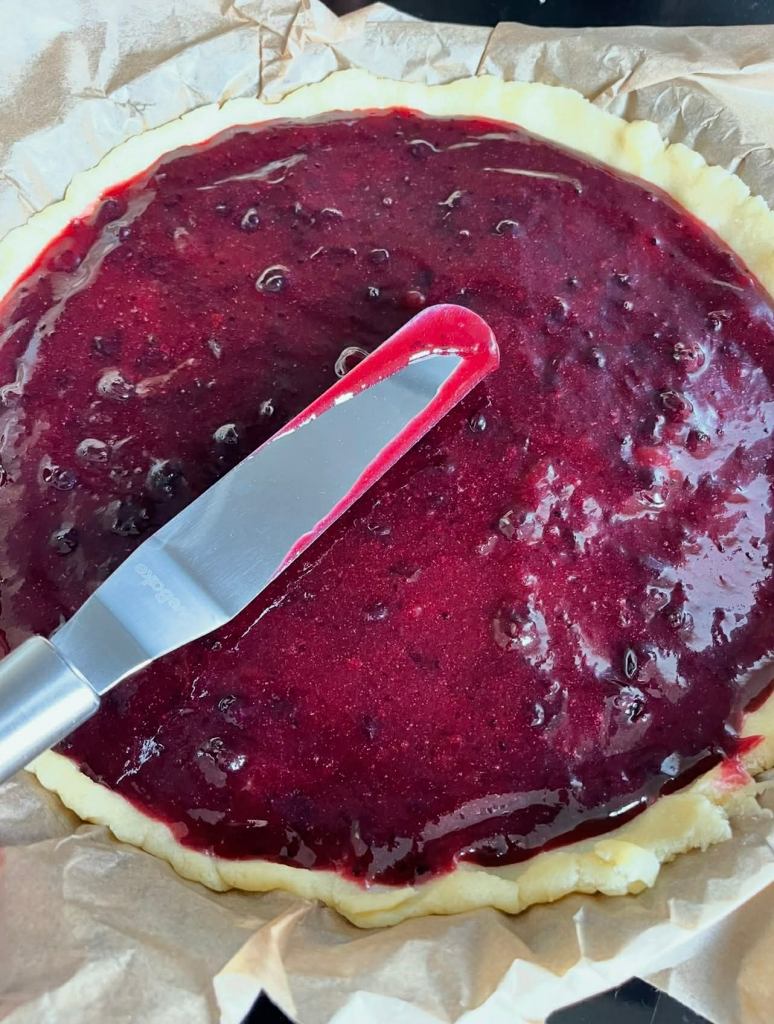 Trupininis pyragas su uogiene, raudona uogienė tepama ant tešlos kepimo formoje