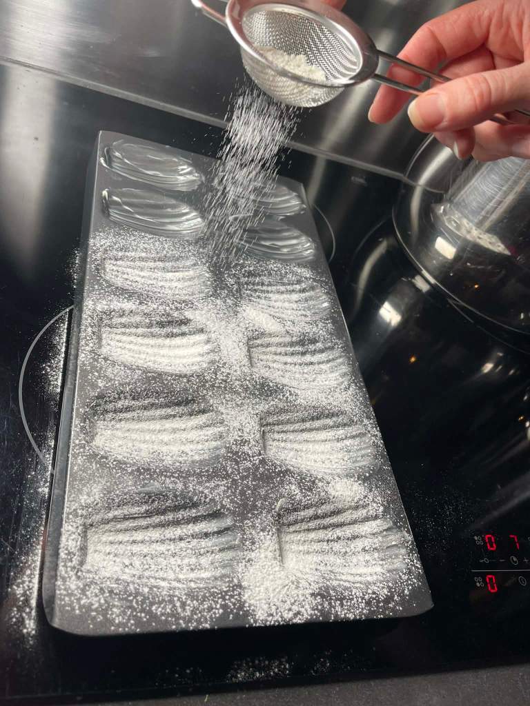 Madlenų formelės išteptos sviestu ir barstomos miltais