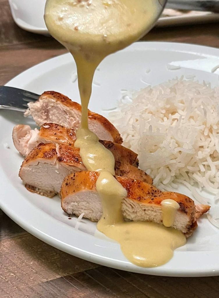 Garstyčių padažas pilamas ant svieste keptos vištienos krūtinėlės supjaustytos lėkštėje prie virtų ryžių.