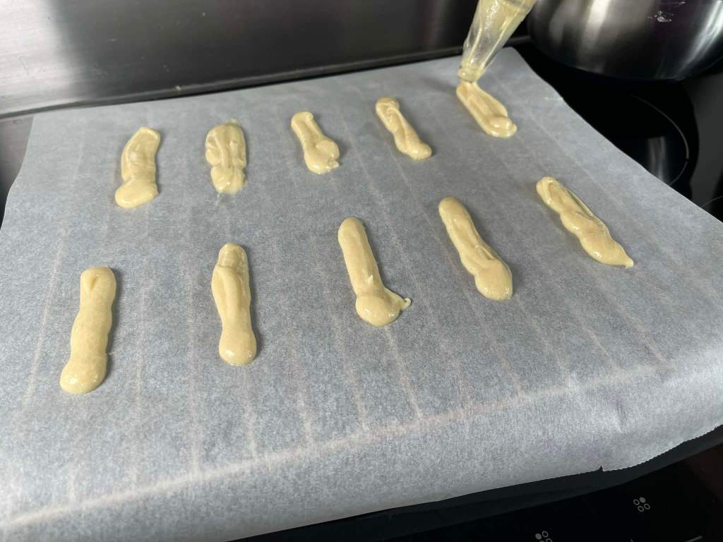 Kačių liežuvėliai, iš konditerinio maišelio spaudžiama tešla ant kepimo popieriaus