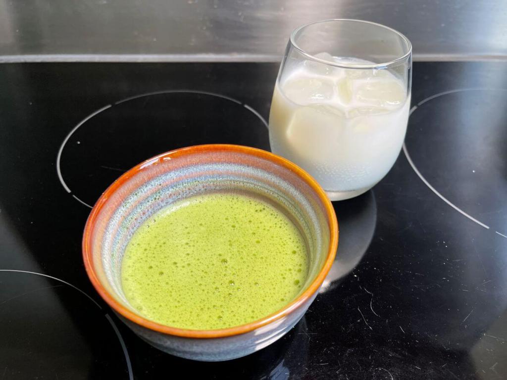 Pienas supiltas į stiklinę su ledukais ir dubenėlyje išplakta matcha su karštu vandeniu paruošti gaminti ledinę matcha latte