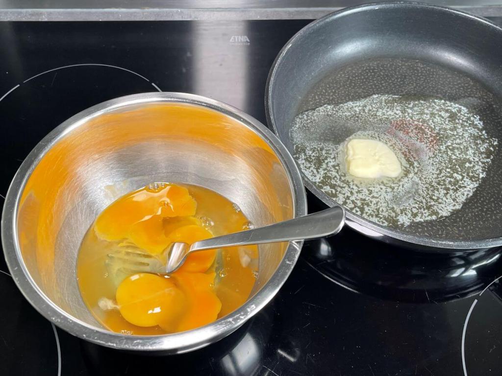 Klasikinis prancūziškas omletas be įdaro, kiaušiniai dubenyje ir tirpstantis sviestas keptuvėje