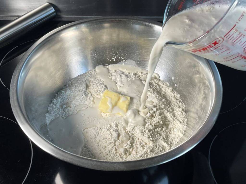 Pienas su mielėmis pilamas į miltų mišinį dubenyje