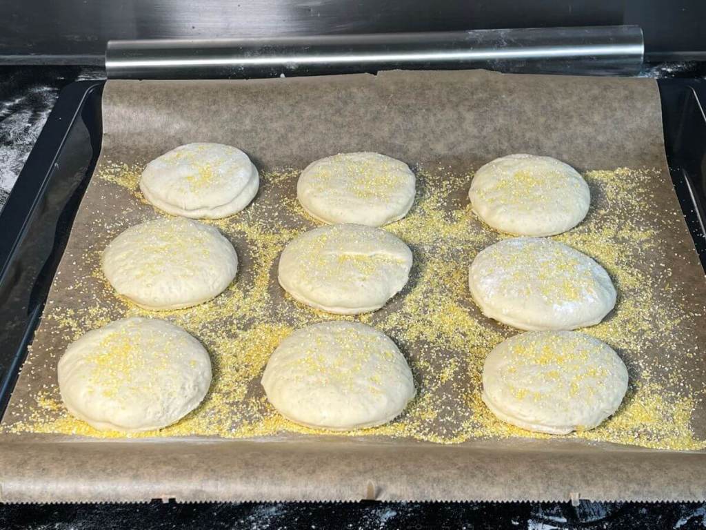 Angliškų mufinų tešlos apskritimai padėti ant kukurūzų kruopomis pabarstyto kepimo popieriaus