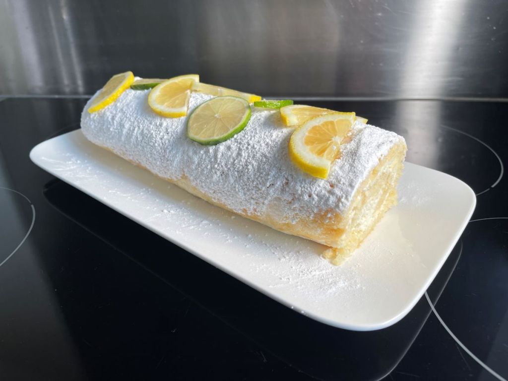 Cukraus pudra ir citrinų bei laimo griežinėliais dekoruotas kreminis citrusinis Génoise biskvitas ant lėkštės.